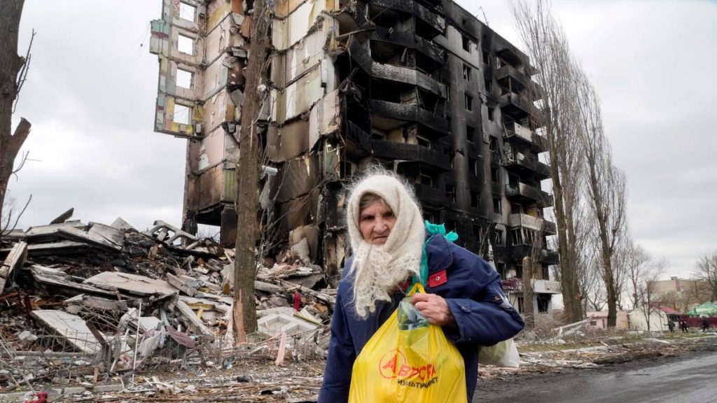 En kvinne går foran to utbrente boligblokker i Borodjanka i Ukraina 6. april
