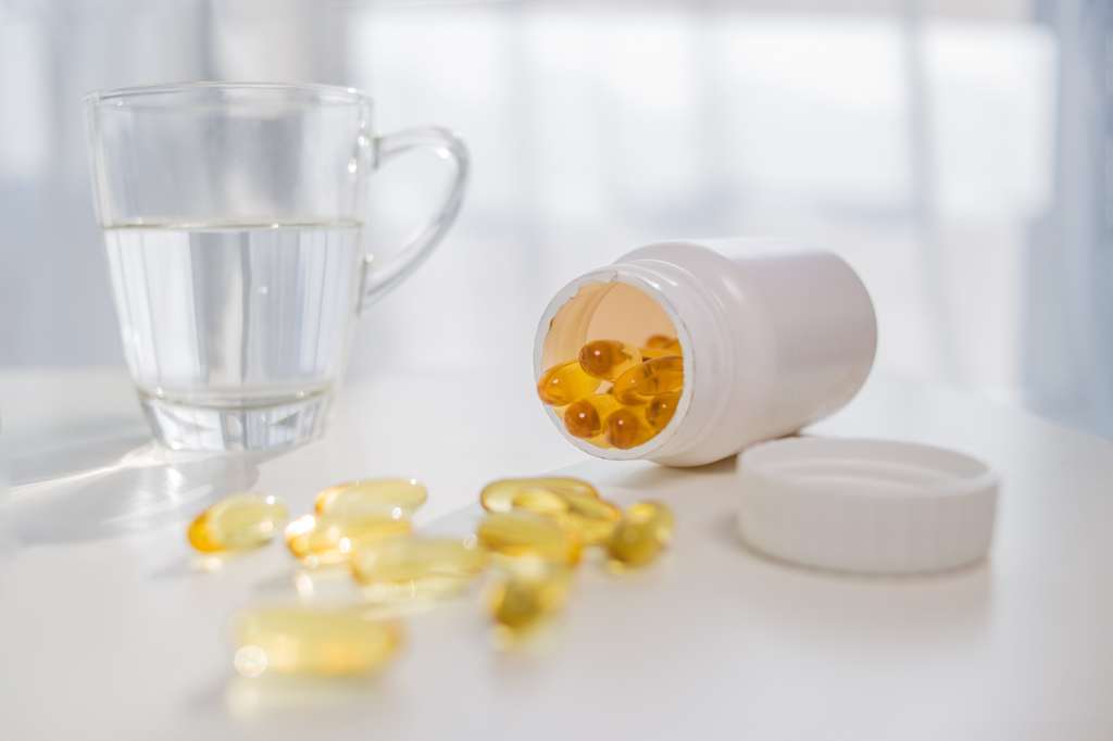 A glass of water next to a jar of vitamin D capsules