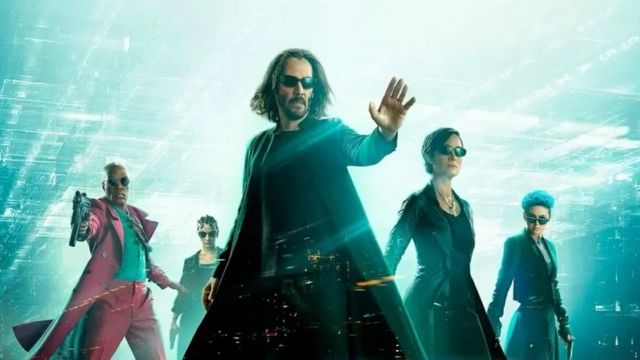 A color photographic montage from the movie The Matrix shows a white man dressed in black with his hand raised;  In the background, a black man and three whites are wearing sunglasses